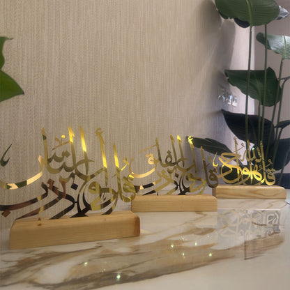 Decorative Arabic calligraphy pieces on wooden stands with a marble surface and plant in the background.