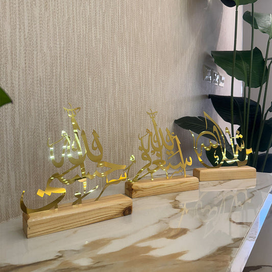 Decorative gold Arabic calligraphy pieces on wooden stands against a textured wall.