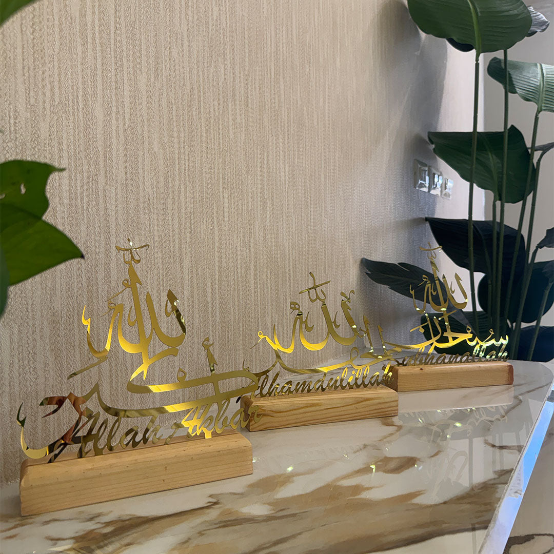 Decorative items with Arabic calligraphy on wooden stands against a neutral wall.