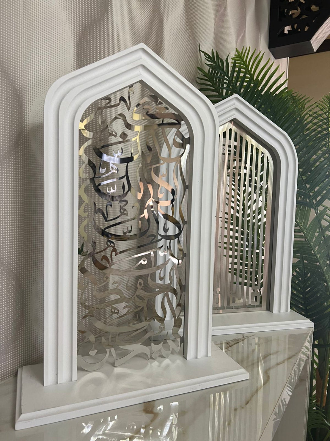 Decorative white arch with intricate cut-out design on a reflective surface.