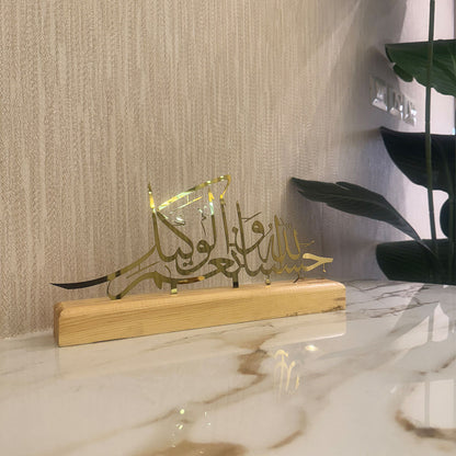 Decorative piece with Arabic calligraphy on a wooden base against a marble wall.