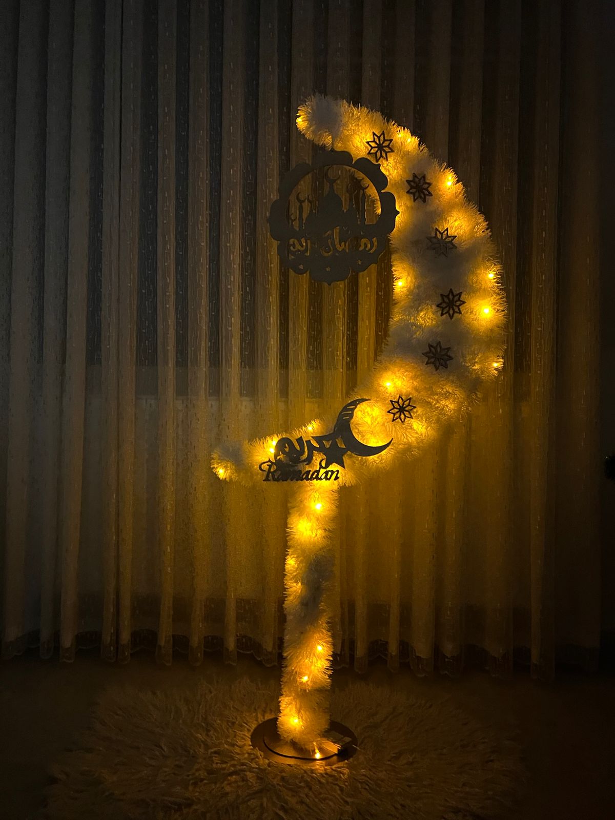 Decorative crescent with lights and star patterns against a curtain background