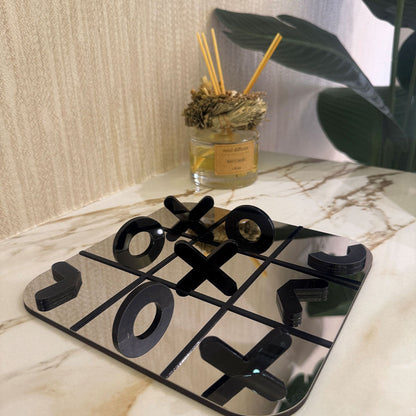 Decorative tic-tac-toe board with black pieces on a marble surface, next to a diffuser bottle.