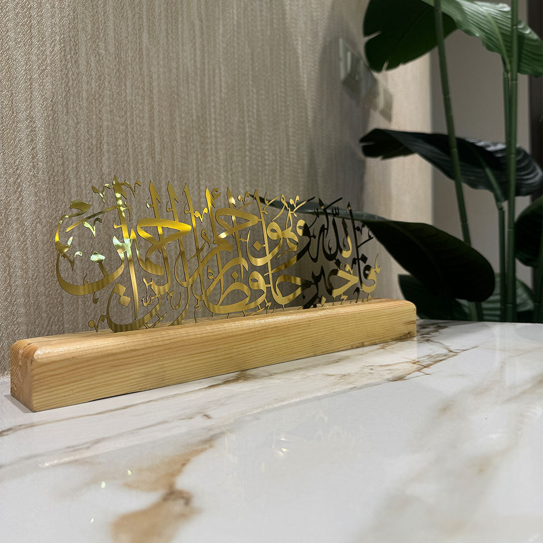 Decorative piece with gold and black calligraphy on a wooden base, placed on a marble surface.