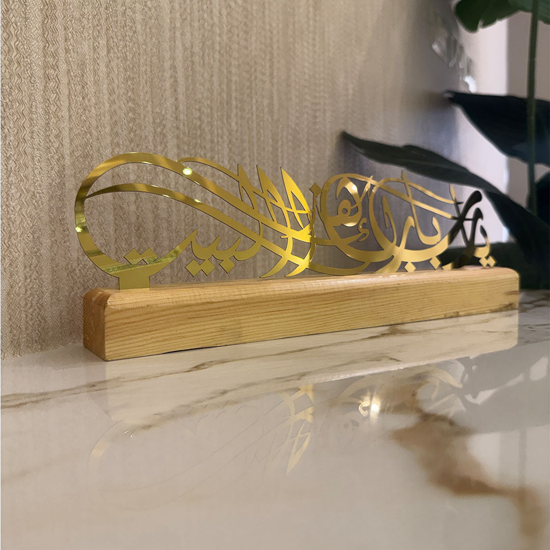 Decorative item with gold Arabic calligraphy on a wooden base against a neutral background